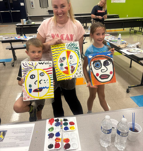 Mom standing with her two girls, each holding a painting they created at family night at Leman Academy in Sierra Vista.